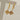 Gold owl-shaped earrings on a clear stand against a neutral background