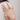 Hand wearing a gold ring with a green gemstone against a neutral background