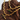 A gold-colored necklace with a wavy chain design and a green gemstone pendant, displayed against a rustic wooden backdrop.