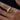 A close-up of a gold ring with a teardrop-shaped polished metal piece and a round abalone shell inlay, worn on a person's finger against a dark background.