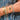 Close-up of a wrist wearing multiple gold and turquoise bracelets on a blue patterned fabric background.