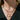 Close-up of a person wearing multiple gold necklaces with a black pinstripe suit background