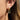 Close-up of an ear wearing gold hoop earrings with chain and gemstone details.