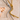 Two necklaces, one silver and one gold, on a textured beige surface with a shell.