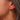 Gold hoop earring with lightning bolt charm worn by a person.