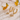Gold hoop earrings with bow-shaped charms on a textured surface with blurred flowers in the background