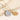 Two gold necklaces with intricate pendants on a textured beige surface