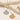 Two ornate necklaces, one gold and one silver, on a textured beige surface.