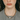 Person with wet hair wearing a gray blazer and necklace against a plain background