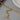 Gold chain necklace on a gray surface with a white plate and brown object in the background