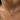 A close-up of a delicate silver chain necklace with a small heart-shaped clear gemstone pendant, worn on a model's neck.