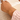 Gold bracelet with a heart-shaped design on a wrist, wearing a pink sweater.