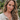 Woman with long, wavy hair wearing a white blouse with lace details outdoors.