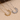 Two sun-shaped necklaces, one gold and one silver, on a textured beige surface.